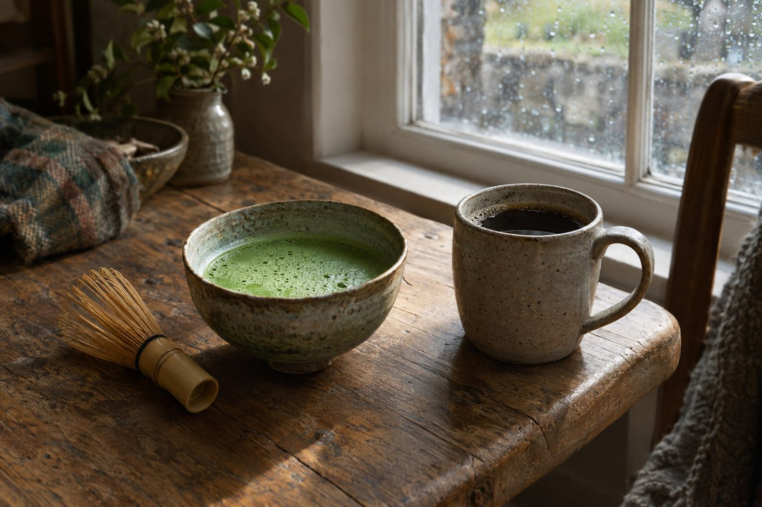 Bowl of bright green matcha and mug of dark coffee side by side on an oak table