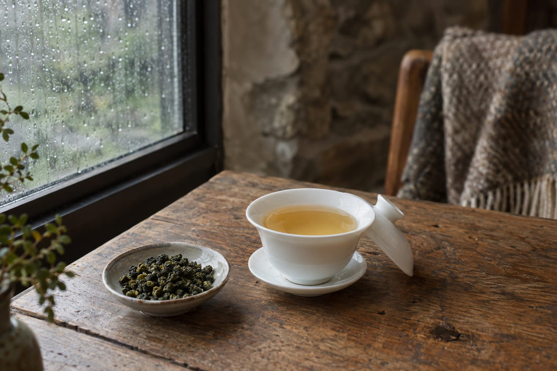 Pale golden milk oolong tea in a white gaiwan with rolled oolong leaves on an oak table