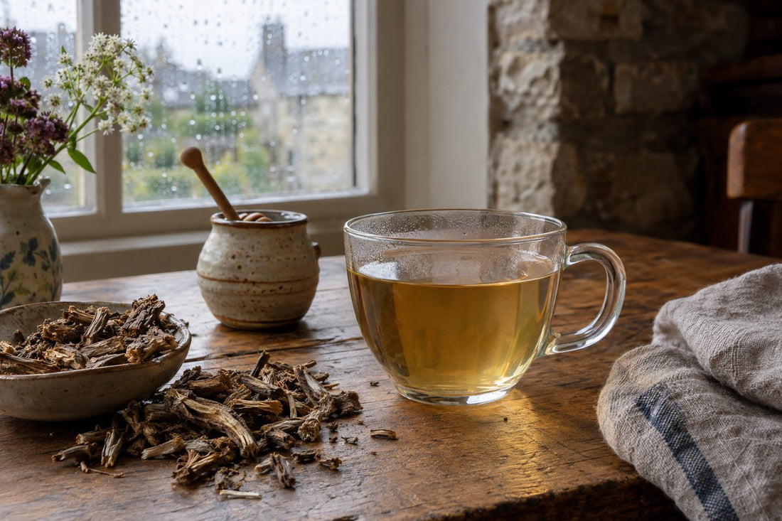 Dried valerian root and a glass cup of pale amber valerian tea on an oak table