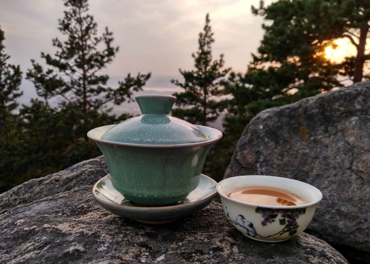 Tea set on a rock with a scenic background of trees and sunset.