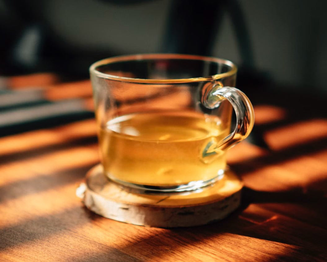 Clear glass mug with tea on a wooden table with sunlight casting shadows