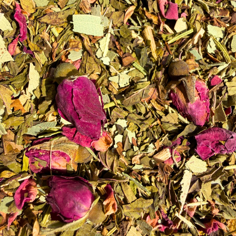 Close-up of chopped green herbs and pink rosebuds in Focus herbal infusion