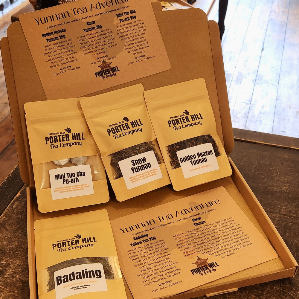 An open kraft cardboard gift box containing five Porter Hill Tea Company Yunnan tea pouches and two printed tea information cards, photographed on a wooden surface.