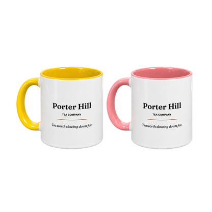 Two Porter Hill tea mugs, one yellow and one pink, with white exteriors and matching coloured handles and interiors